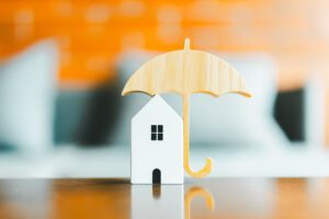 Model of umbrella with house on wooden table concept of the system of insurance savings and Housing insurance against impending loss and fire, building fire insurance concepts