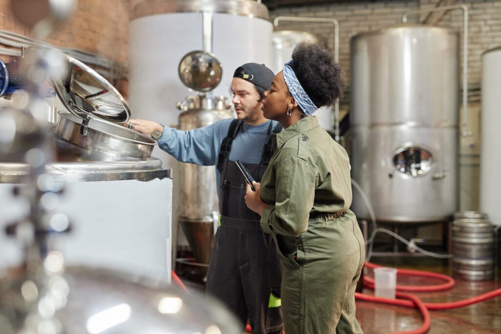 Female Process Supervisor and Factory Worker Monitoring Cider Production Indoors