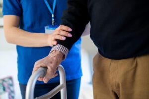 care home nurse helping elderly man walk