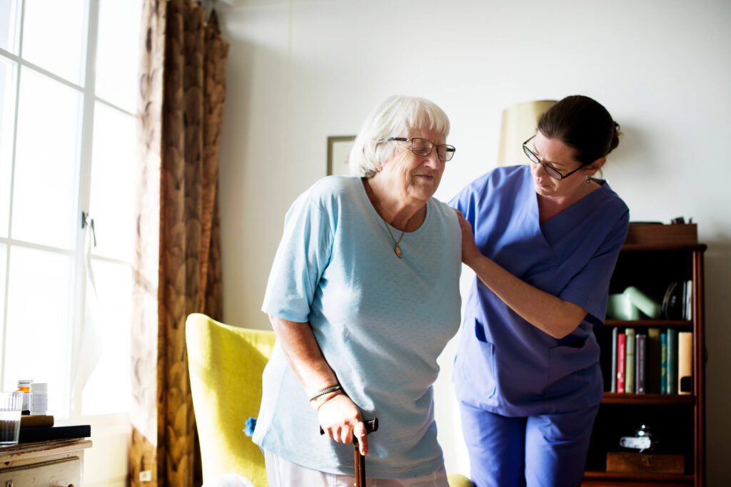care home nurse helping elderly woman stand